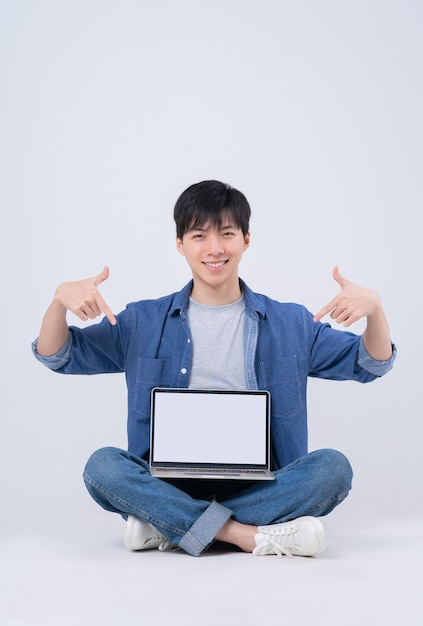 Young Asian man sitting and using laptop on white background