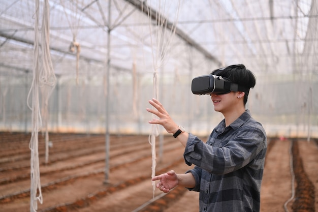 Young asian man smart farmer standing in greenhouse and wearing visual reality glasses technology.