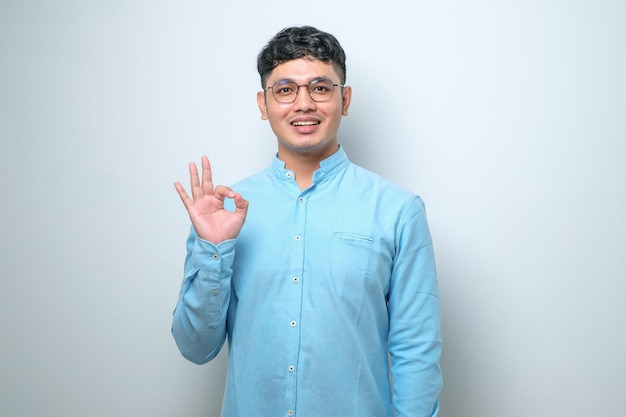 Young Asian man smiling and doing ok sign with fingers excellent symbol