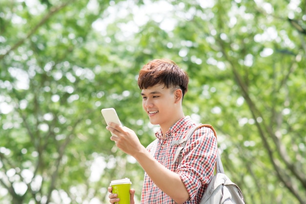 Young asian man smiling and using phone in park