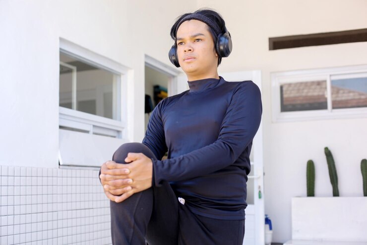 Photo スポーツウェアを着たアジア人の若者がヘッドフォンを使って走る前に足を伸ばしている