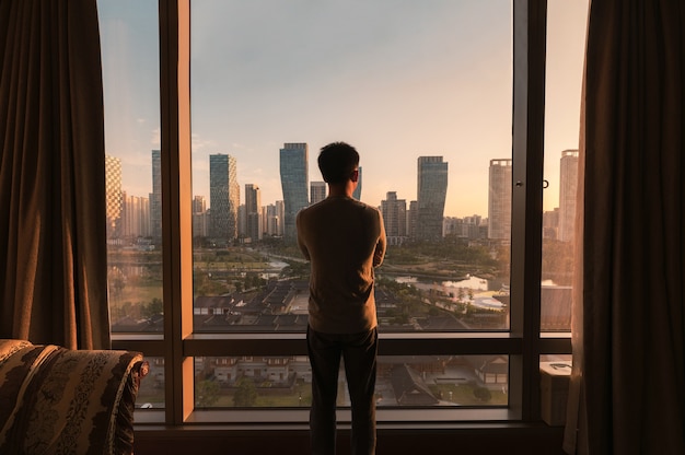 Photo young asian man standing and looking through window in a hotel