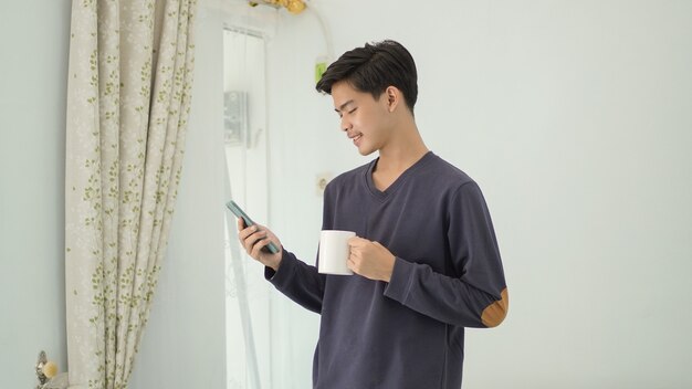 Young asian man standing playing smartphone while holding a drink