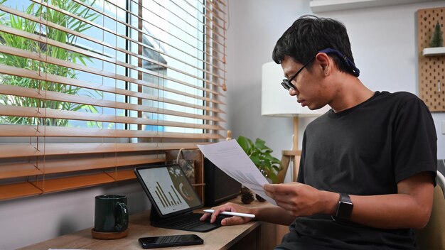 Young asian man stock trader checking and analyzing financial graph on tablet computer