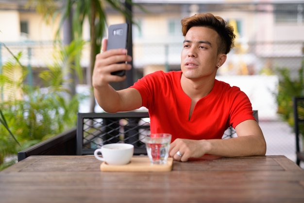 屋外のコーヒーショップで自分撮りをしている若いアジア人男性