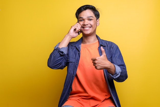 Young Asian man talking on the phone while showing thumbs up with happy expression