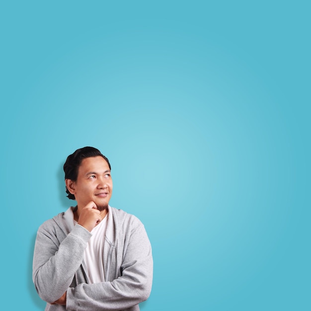 Young Asian man thinking expression eyes glance to the top over blue background with copy space