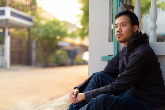 야외 거리에 앉아있는 동안 생각하는 젊은 아시아 남자