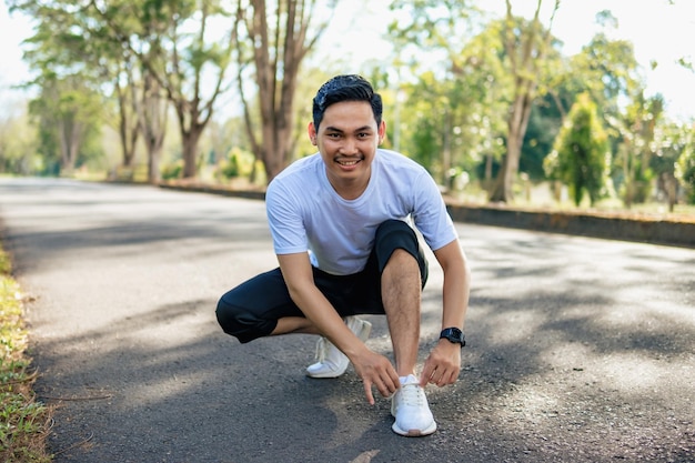 Giovane uomo asiatico che si lega le scarpe preparandosi per correre nella natura stile di vita sano