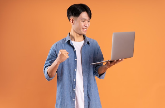 Young asian man using laptop on brown background