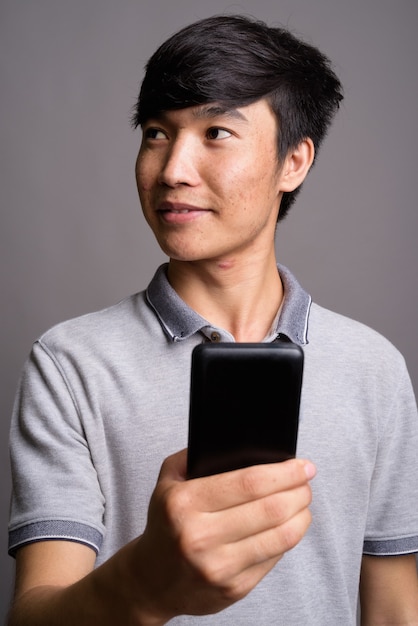 Young Asian man using mobile phone against gray wall