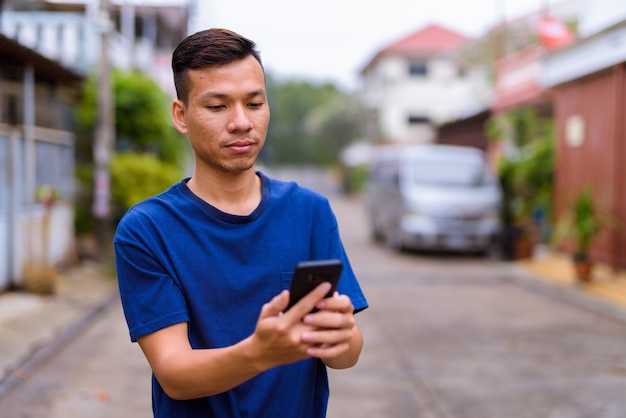 屋外の通りで電話を使用して若いアジア人男性