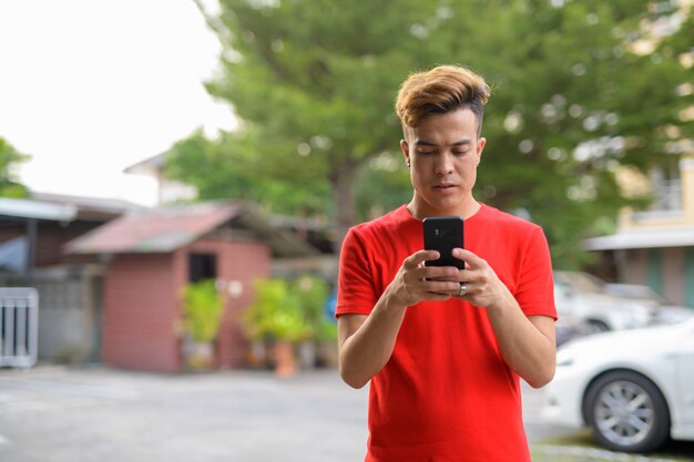 屋外の通りで電話を使用して若いアジア人男性