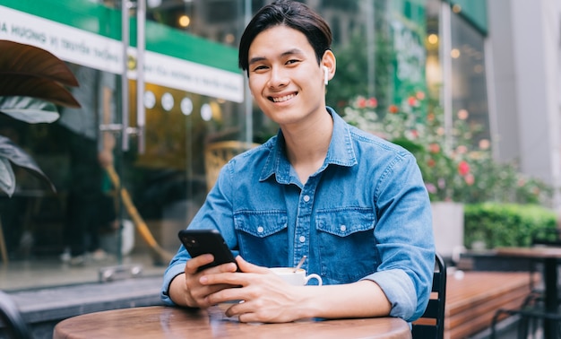 写真 コーヒーショップでスマートフォンを使用して若いアジア人男性