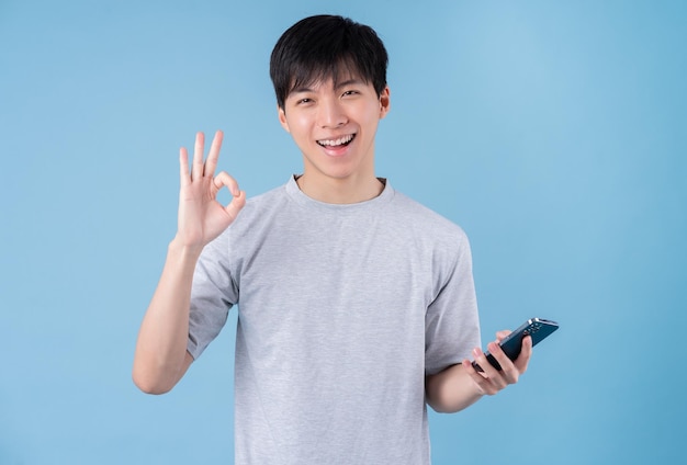 Young Asian man using smartphone on blue background