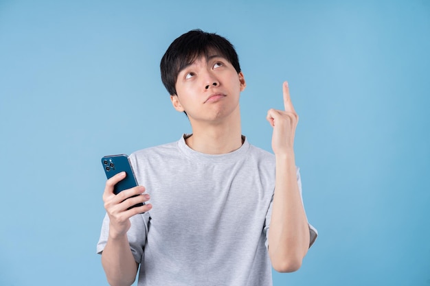 Young Asian man using smartphone on blue background