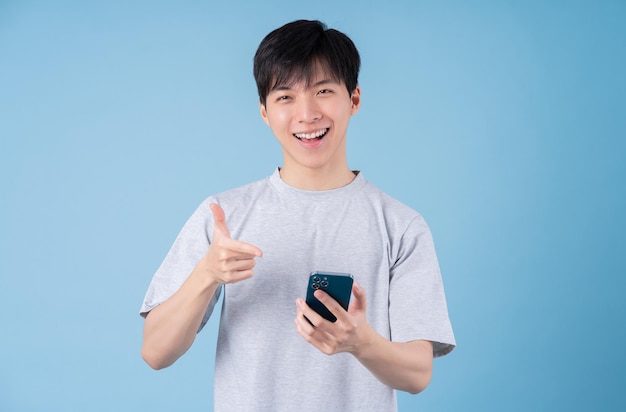 青の背景にスマートフォンを使用して若いアジア人