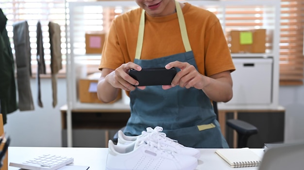 Young Asian man using smartphone take a photo of shoes for upload to website online shop