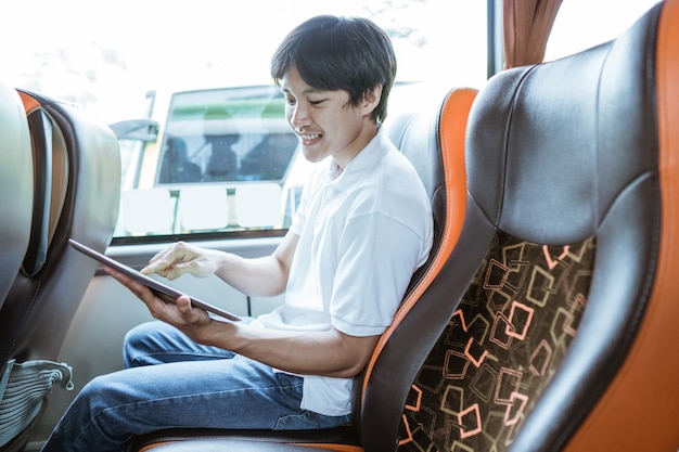 A young asian man using a tablet while sitting on the bus