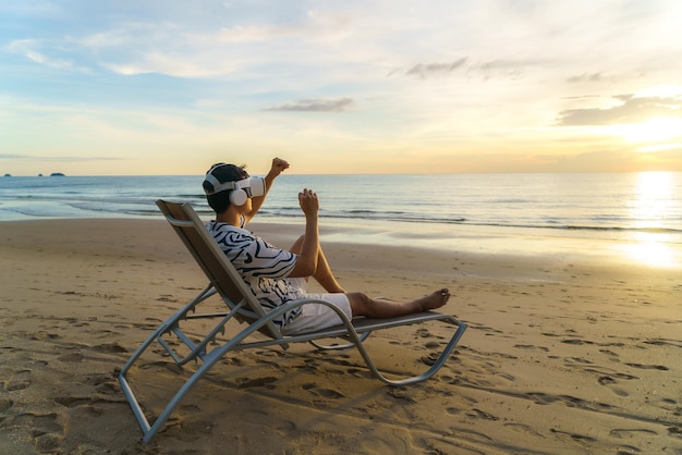 Young Asian man using virtual reality glasses for business meeting on the tropical beach over beautiful sea and sky background