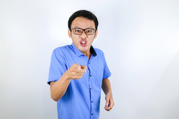 Young Asian Man wear blue shirt is funny angry face with shouting and pointing finger at camera isolated over white background