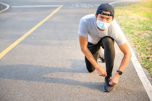 Young asian man Wear a fitness mask Run in the park Sweating from a morning workout concept: wear a mask against SARS-Cov-2.