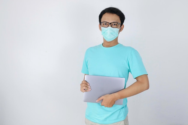 Young Asian Man wear medical mask is carrying a laptop Indonesian man wearing blue shirt