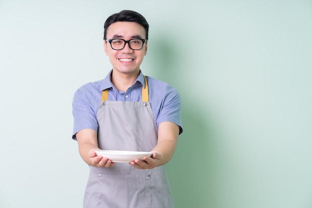 緑の背景にポーズをとってエプロンを身に着けている若いアジア人男性