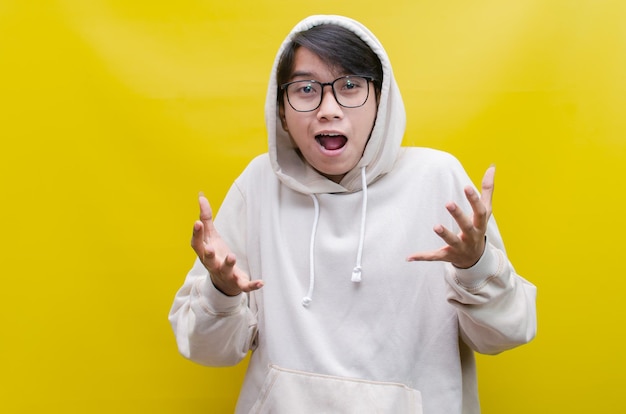 a young Asian man wearing beige hoodie with surprised and shocked expression opening his arms