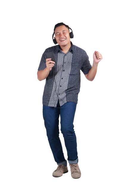 Photo young asian man wearing blue jeans and batik shirt listening to music and dancing happily