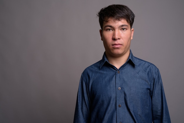 Young Asian man wearing blue shirt against gray wall