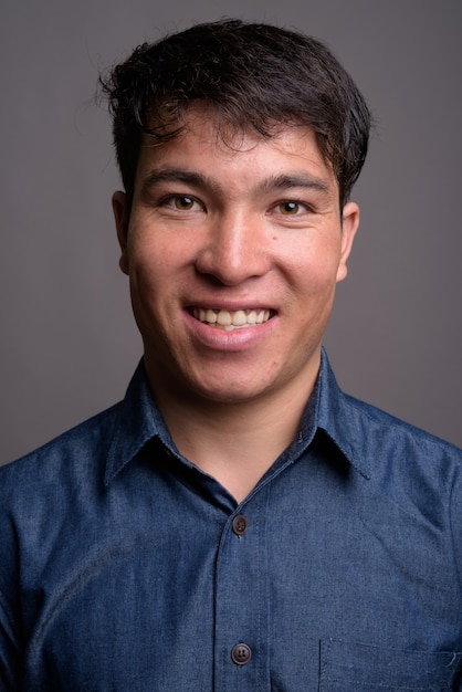 Young Asian man wearing blue shirt against gray wall