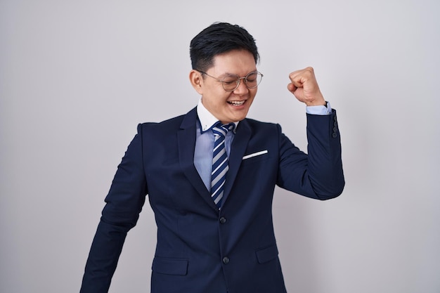 Young asian man wearing business suit and tie dancing happy and cheerful smiling moving casual and confident listening to music