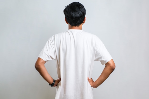 写真 白い背景の上にカジュアルなシャツを着て後ろ向きに立って体に腕を持って目をそらしている若いアジア人男性
