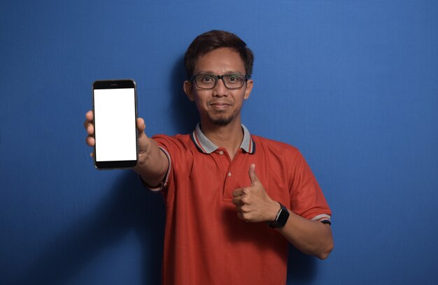 Young Asian man wearing casual tshirt with thumbs up showing blank white smart phone screen