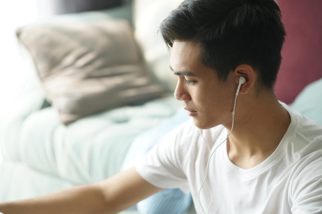 사진 청년 아시아인 남자가 집에서 소파 에서 음악을 듣고 휴식을 취하고 있습니다.