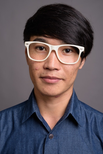 Молодой азиатский мужчина в очках выглядит умным на фоне серой стены