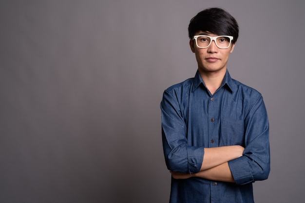 Young Asian man wearing eyeglasses looking smart against gray wall