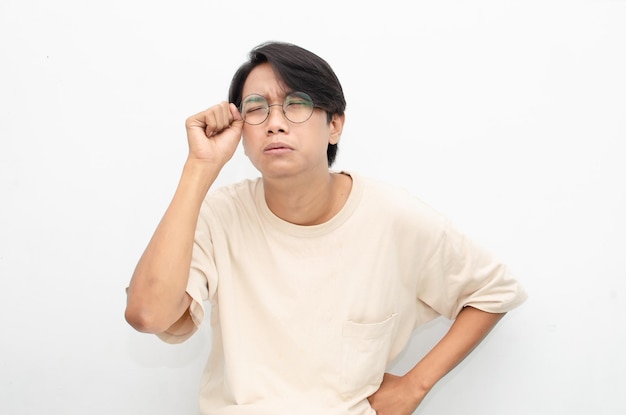 Young Asian man wearing glasses and beige tshirt with crying face expression isolated over white