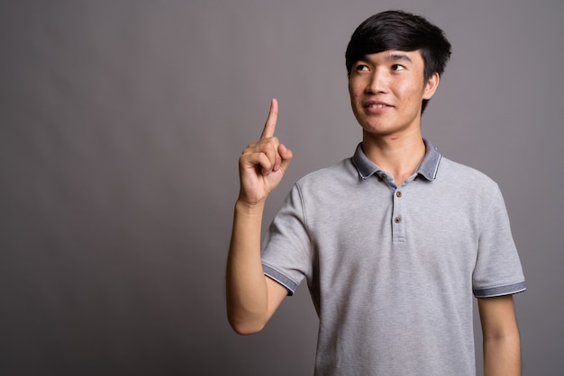 Молодой азиатский мужчина в серой рубашке поло у серой стены