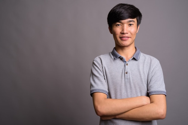 Young Asian man wearing gray polo shirt against gray wall