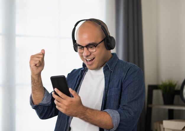 Giovane uomo asiatico che indossa la cuffia e ascolta la musica che tiene smartphone