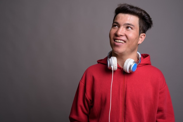 Young Asian man wearing headphones against gray wall