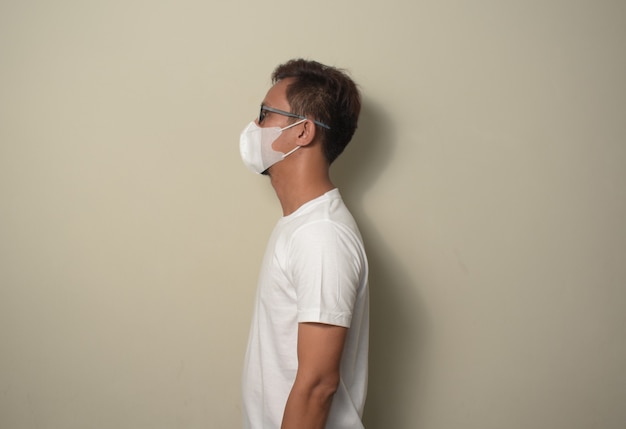 Young Asian man wearing medical mask looking to side relax profile pose with natural face