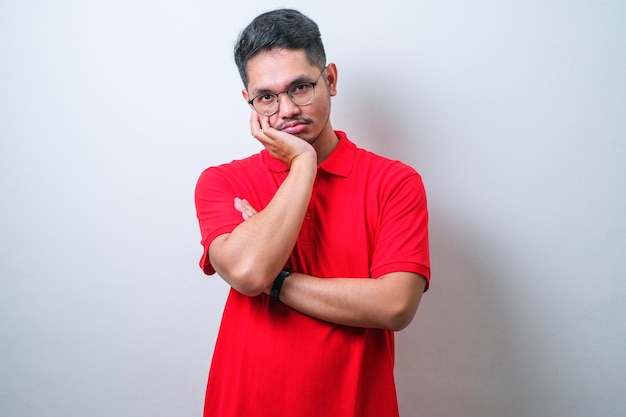 Young asian man wearing red shirt and glasses thinking looking tired and bored with depression problems with crossed arms