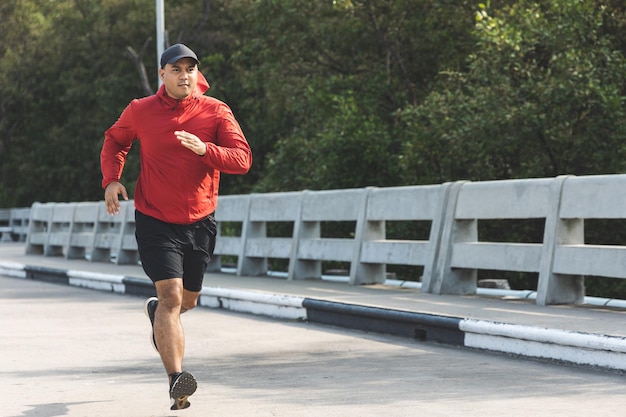 屋外で走っているスポーツウェアを着ている若いアジア人男性。道路でジョギングしているインド人の肖像画。アスリートアウトドアコンセプトのトレーニング。