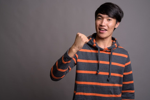 young asian man wearing striped hoodie against gray wall