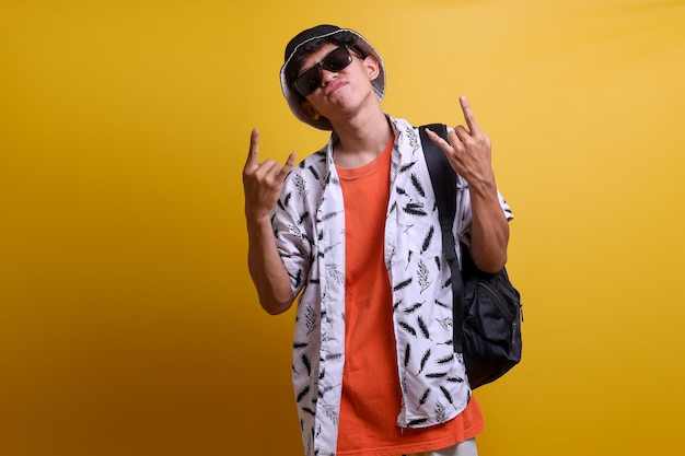 Young Asian man wearing sunglasses showing rock and roll fingers sign while carrying backpack