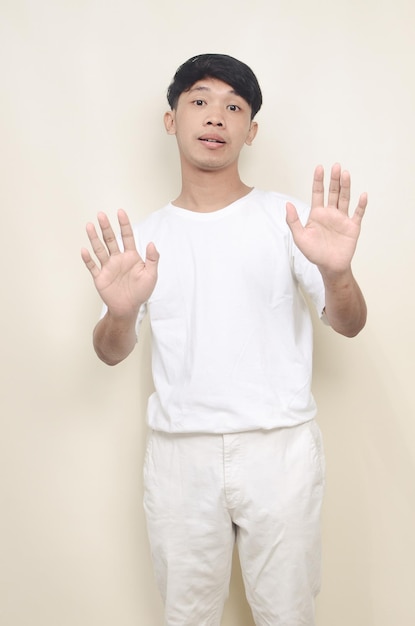 고립된 배경 위에 서서 손바닥으로 노래를 멈추고 서 있는 티셔츠를 입은 젊은 아시아 남자