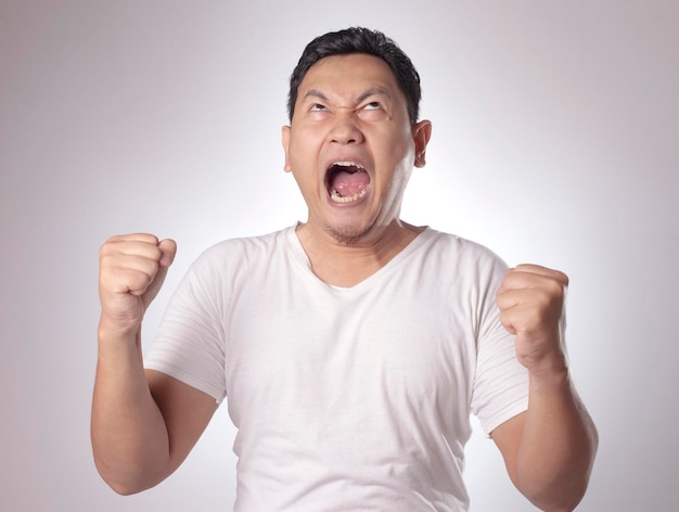 Young Asian man wearing white shirt shouting because of anger Background on gray